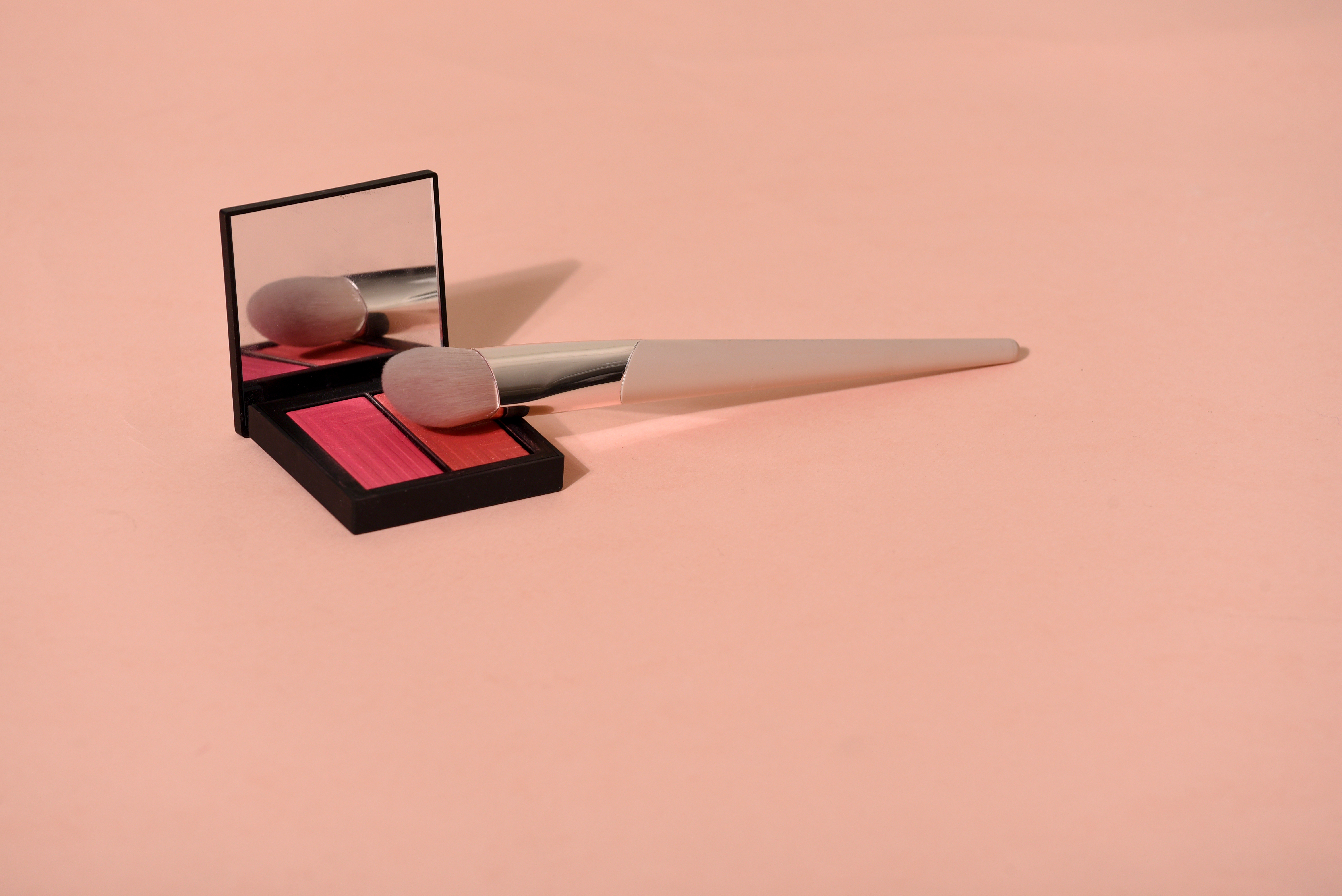 Close-Up Of Blusher With Make-Up Brush On Colored Background