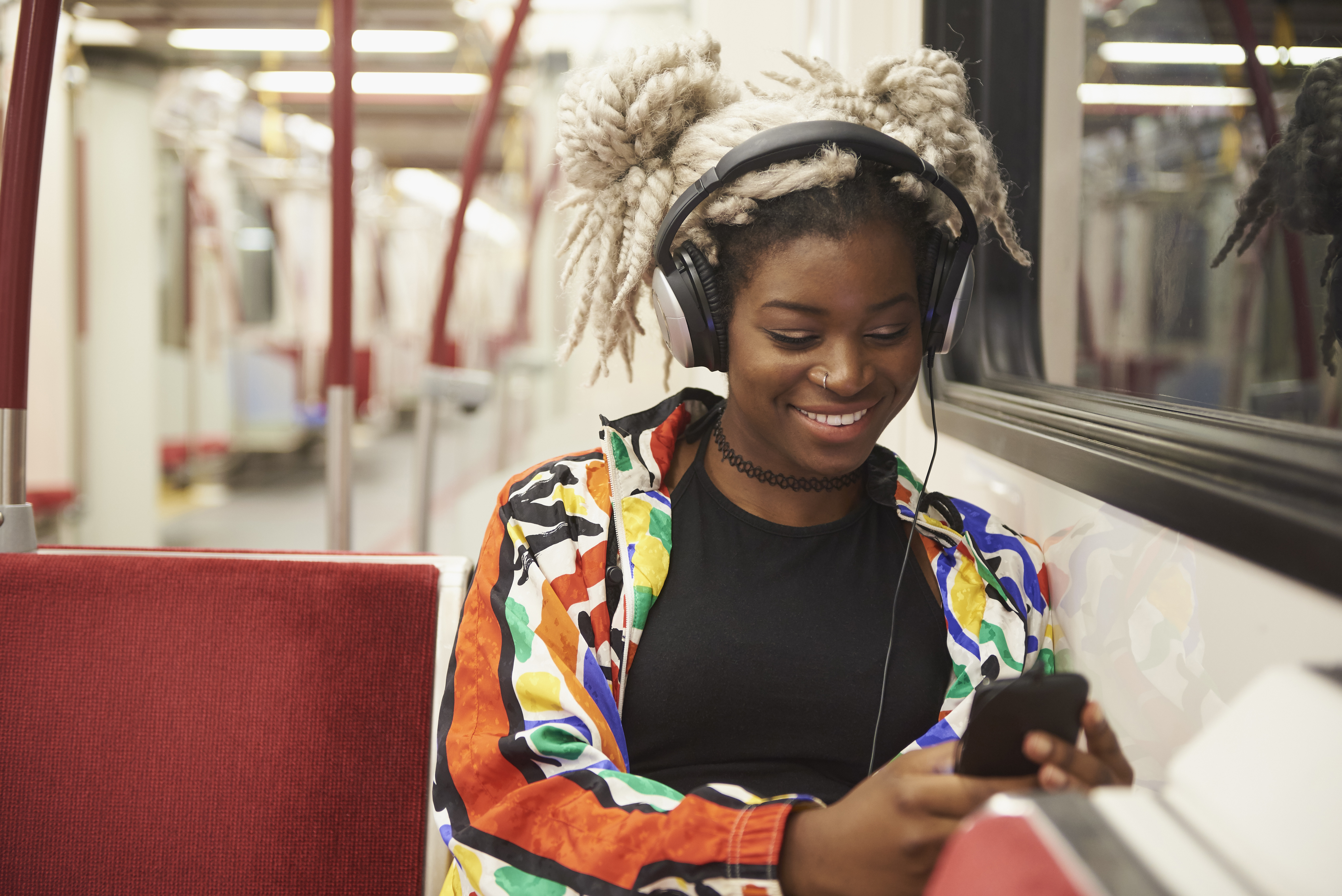 Black woman listening to cell phone with headphones on subway