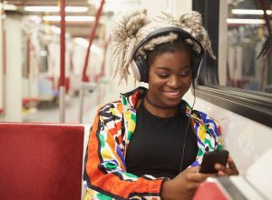 Black woman listening to cell phone with headphones on subway