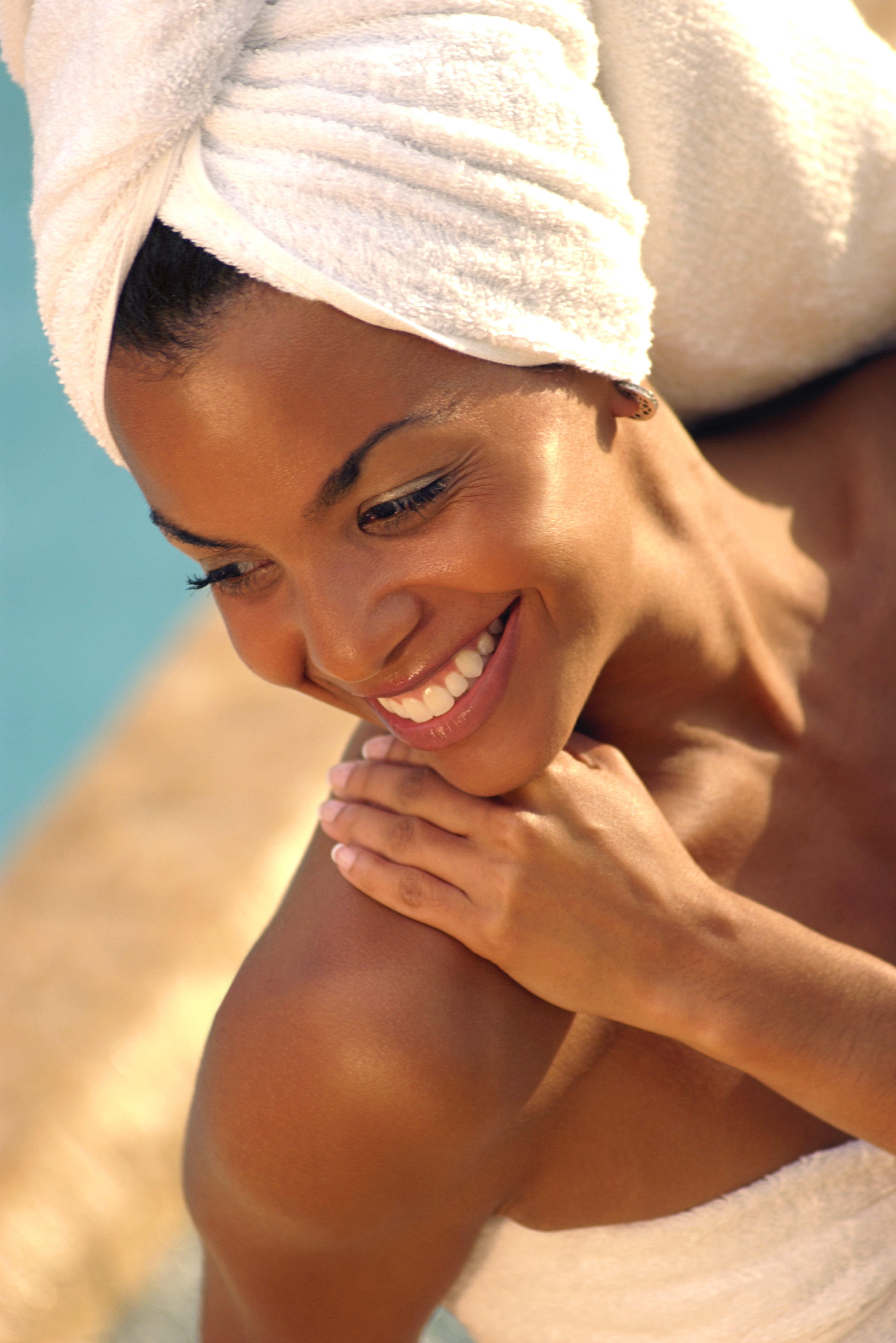 Close-up looking down on a smiling woman with towels wrapped around her hair and body and her hand on her shoulder.