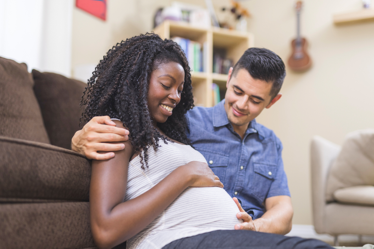 Pregnant African American woman snuggles on the floor in front of the couch with her ethnic husband
