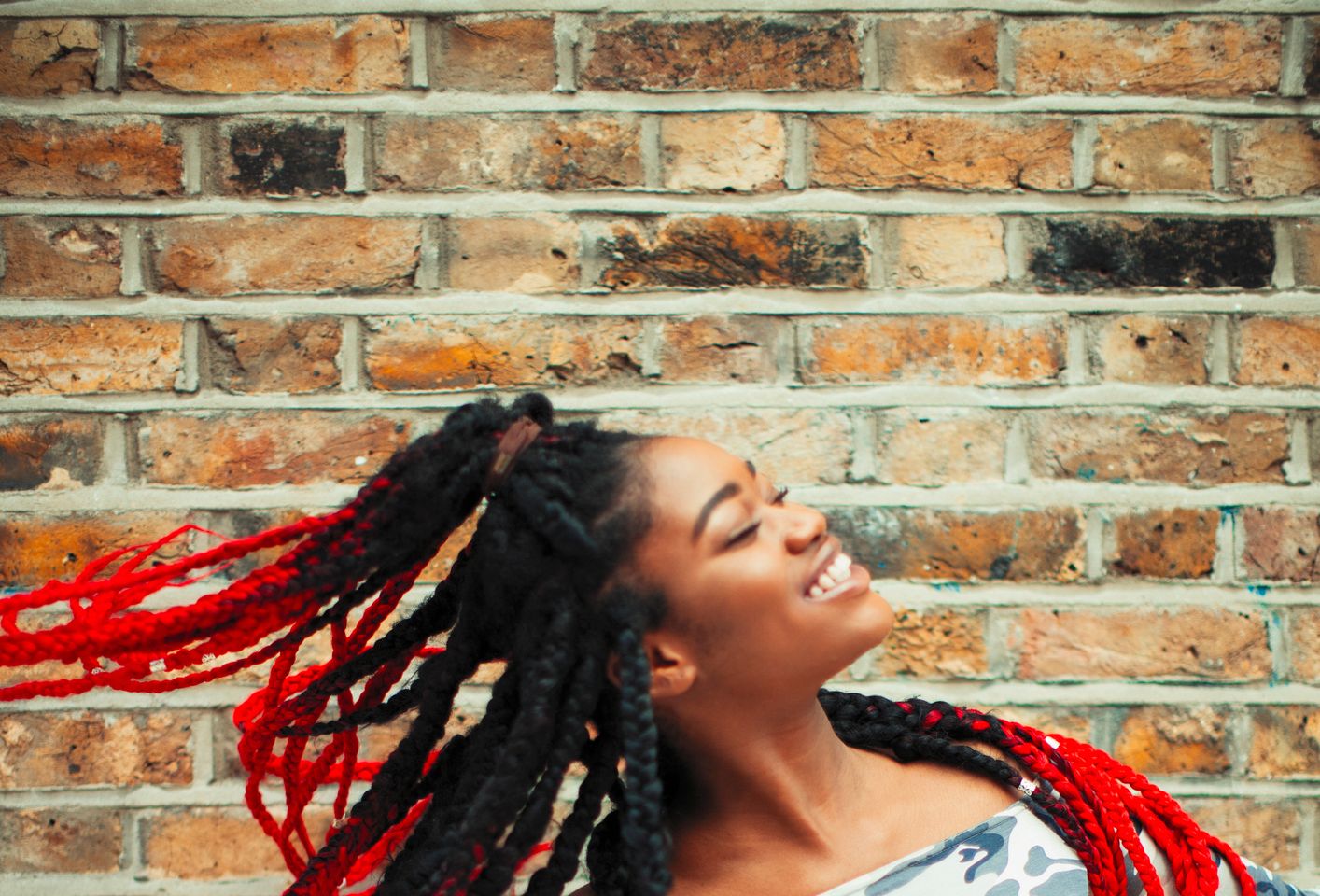 Carefree young woman in camouflage clothing dancing against brick wall