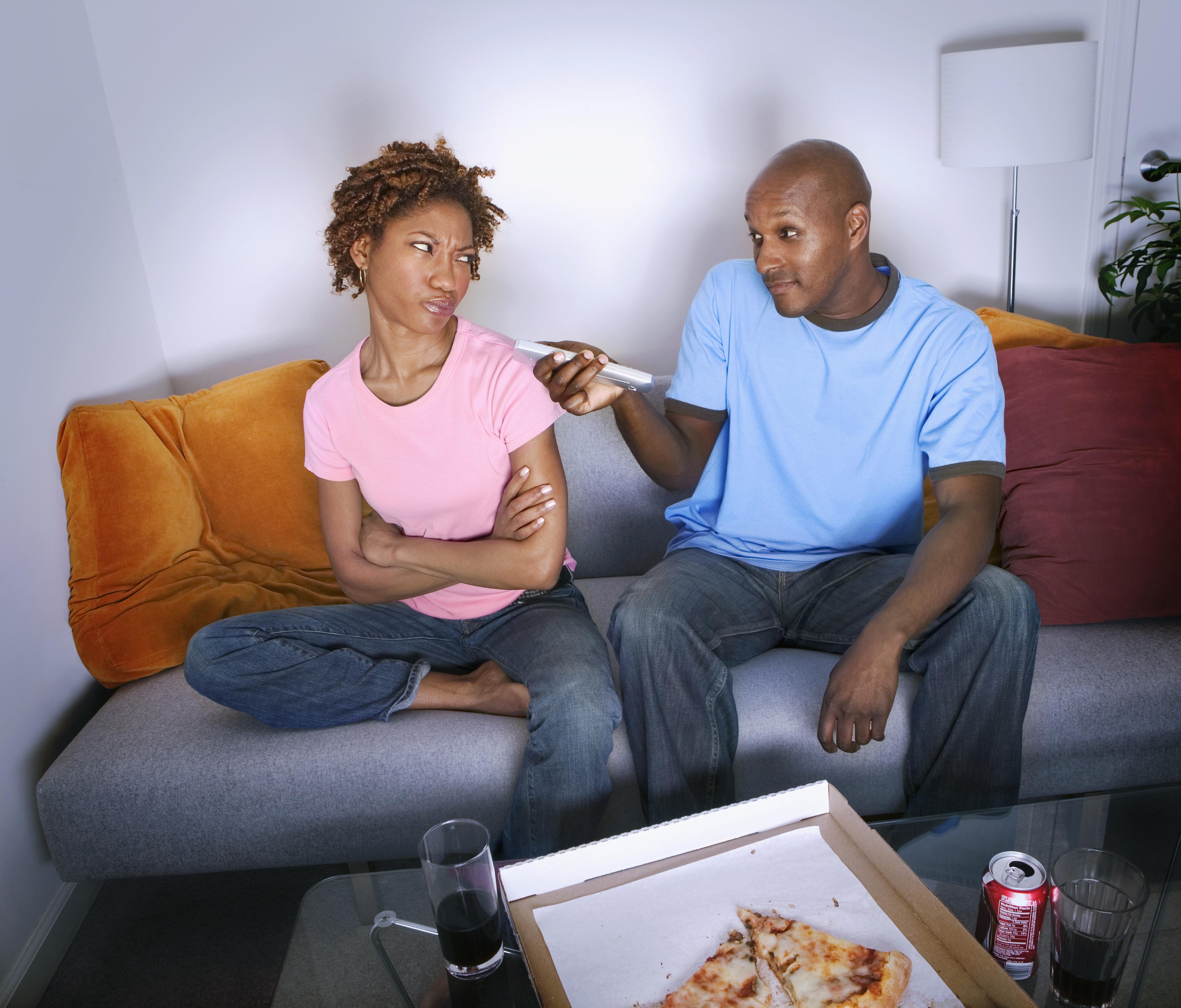 African man pointing remote control at annoyed girlfriend