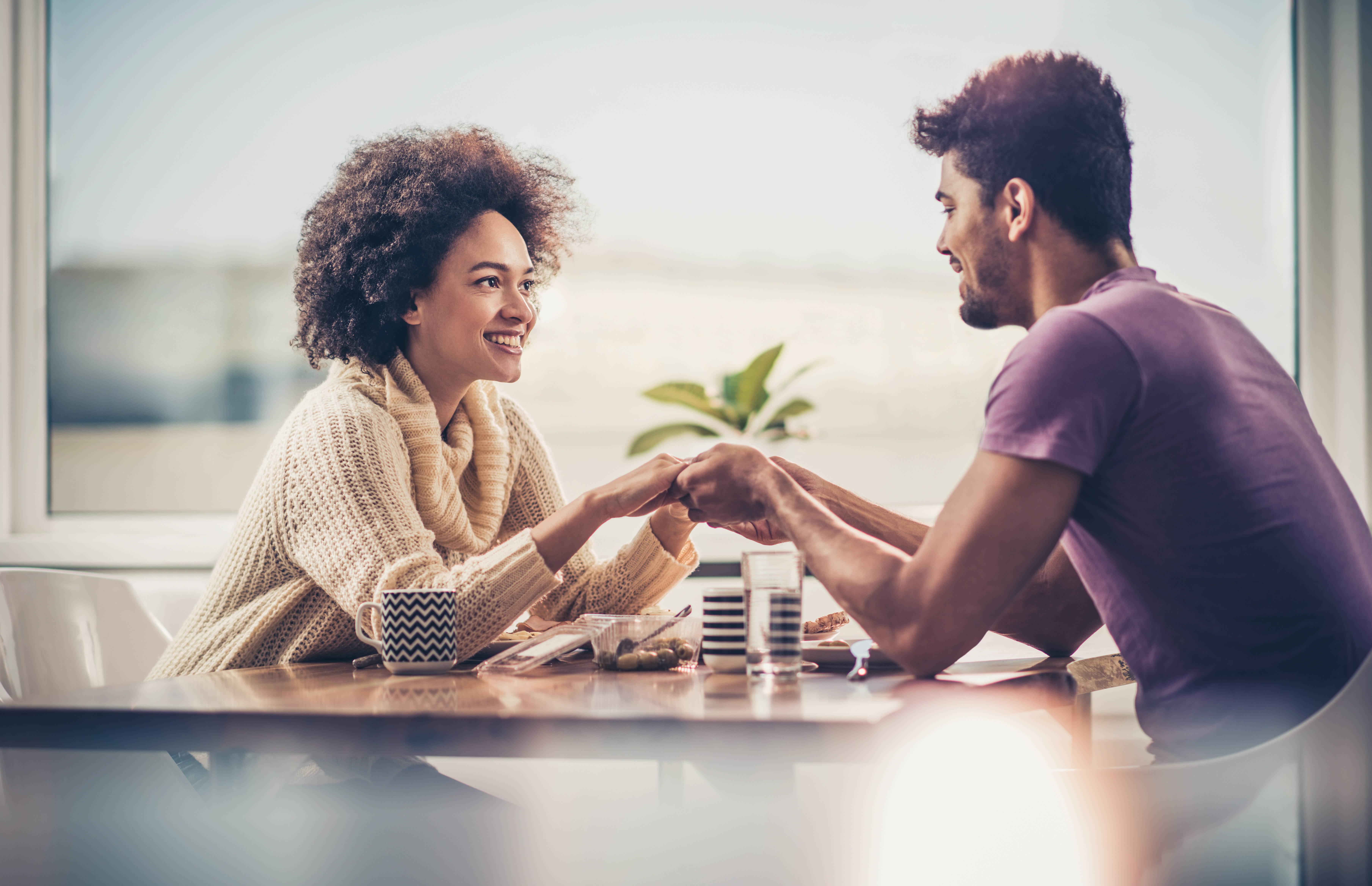 Loving black couple holding hands while having a lunch by the window.