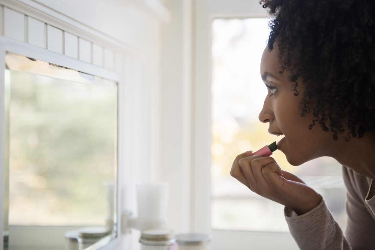 Woman looking in mirror and applying lipstick