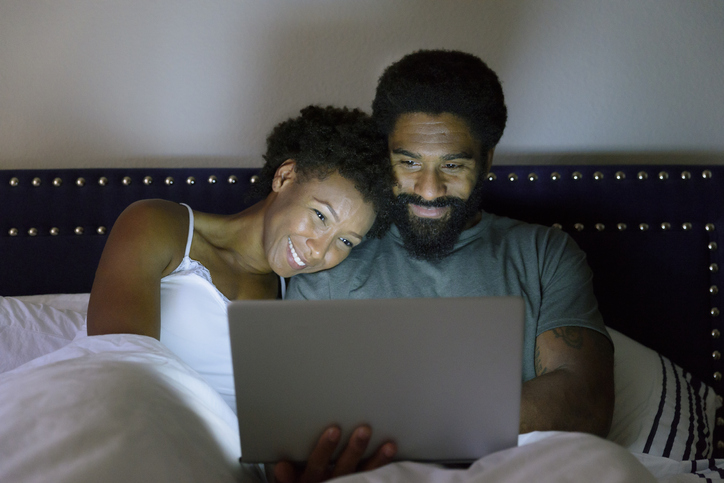 Man and woman in bed looking at lap top computer
