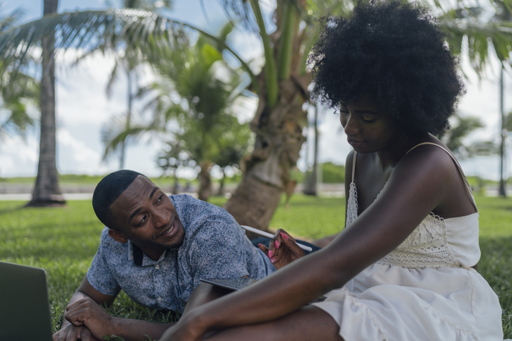 USA, Florida, Miami Beach, young couple using tablet and laptop on lawn in a park