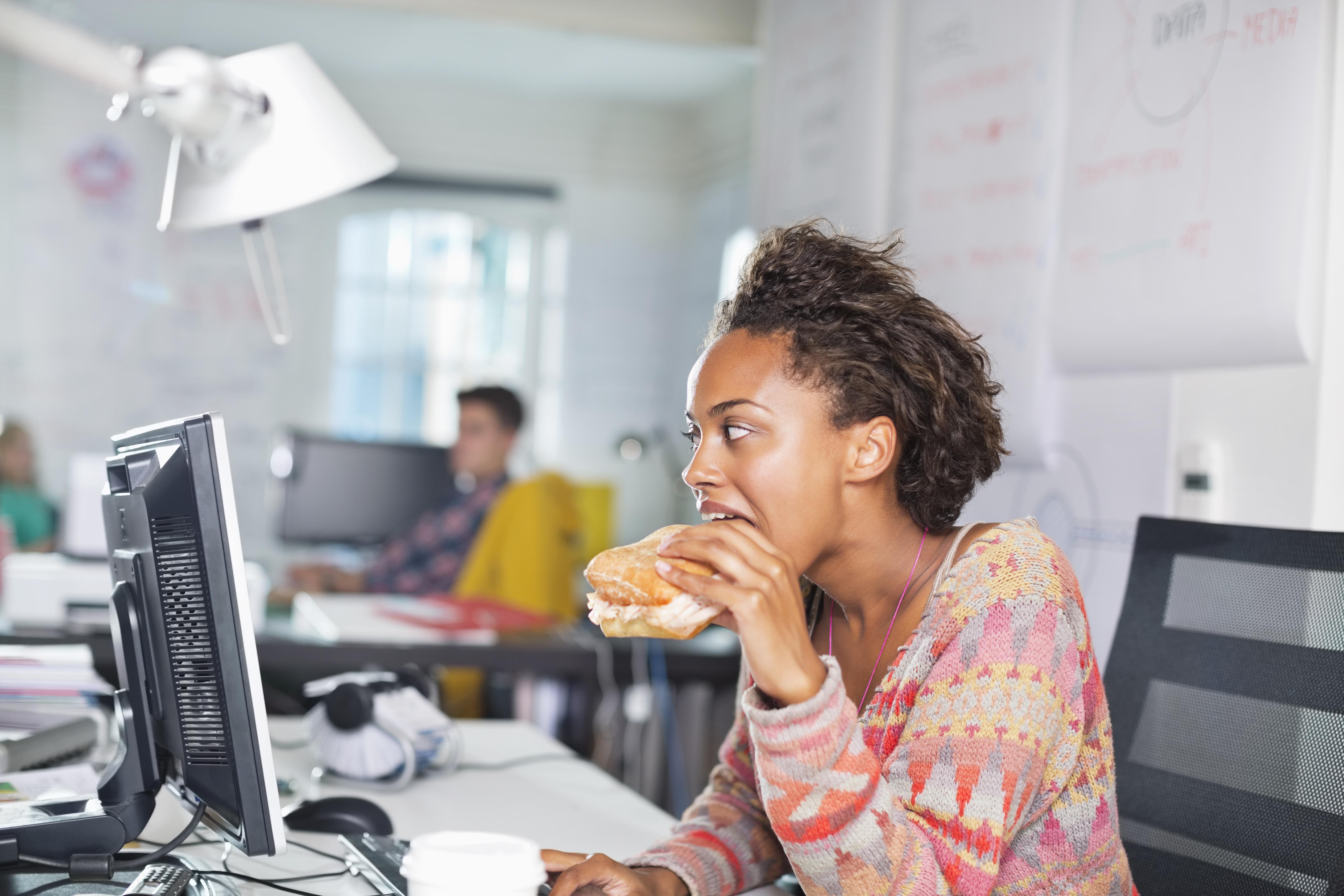Businesswoman eating burger at desk
