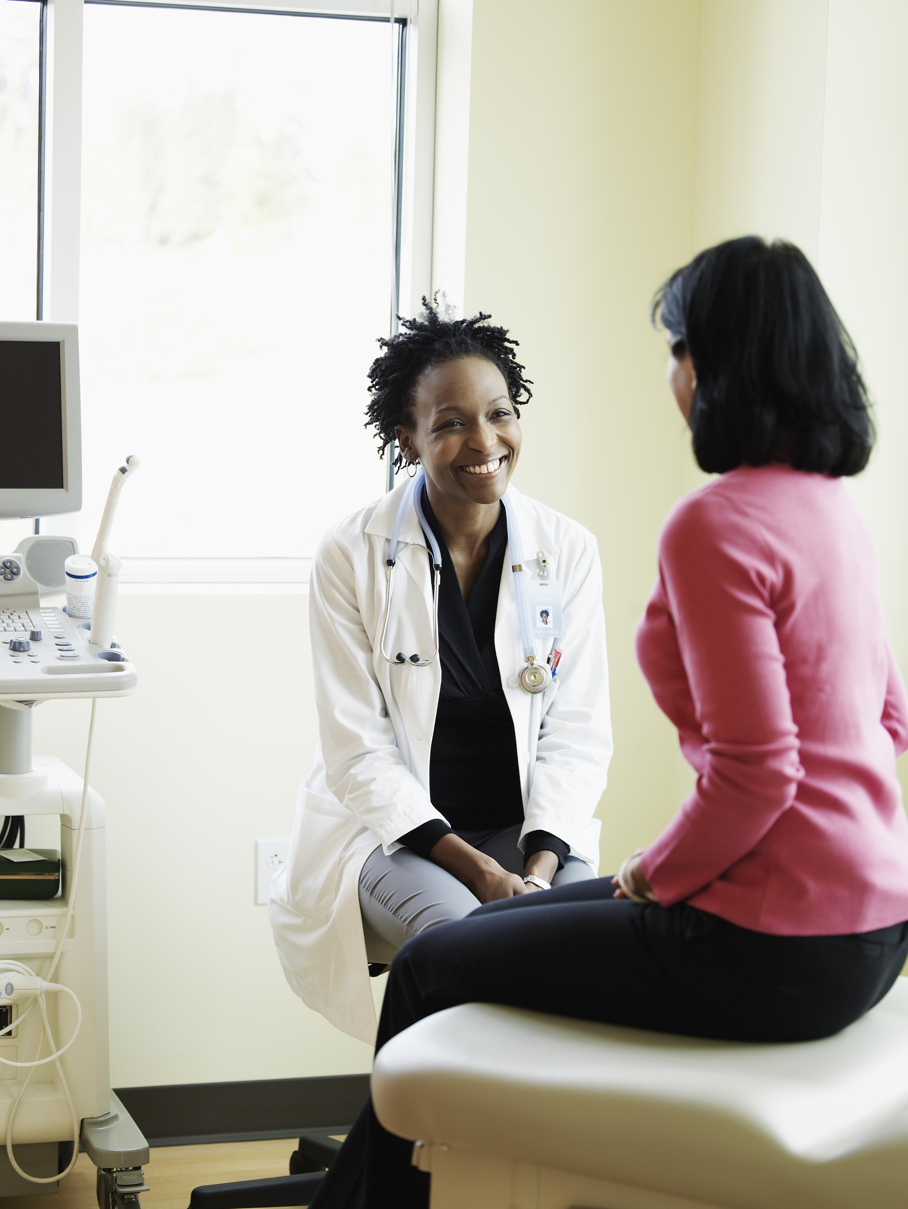 Female doctor talking to woman in exam room, smiling