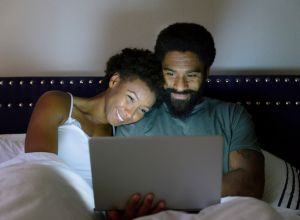 Man and woman in bed looking at lap top computer