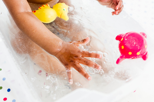 Baby girl (6-11 months) in bath tub playing with colorful toys