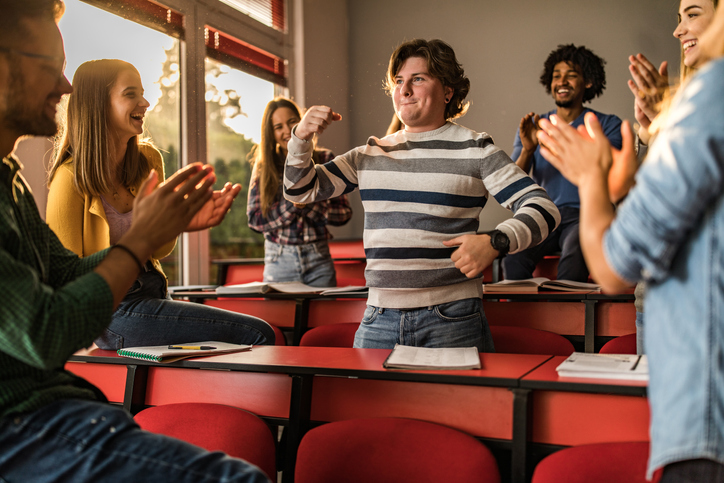 Young students applauding their friend in the classroom.