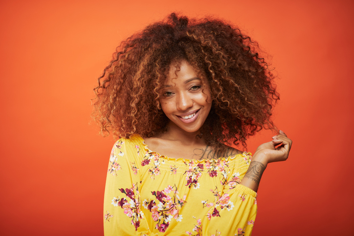 Beautiful afro Caribbean young woman in summer clothes against orange background.