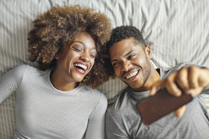 Smiling couple taking selfie on smart phone in bed