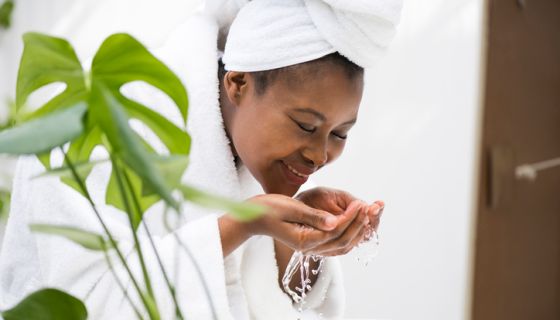 Young African woman washing her face in a bathroom, skincare