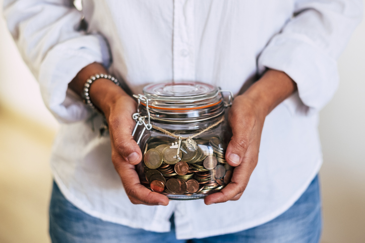Midsection Of Woman Holding Coins In Jar At Home