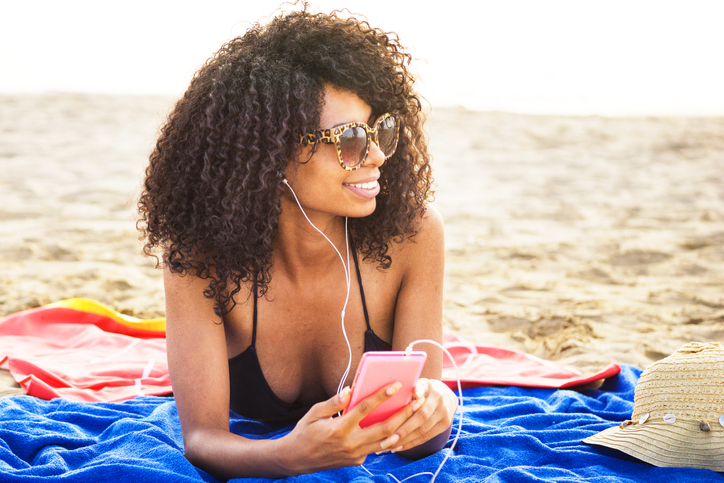 Smiling Young Woman Listening Music While Lying At Beach