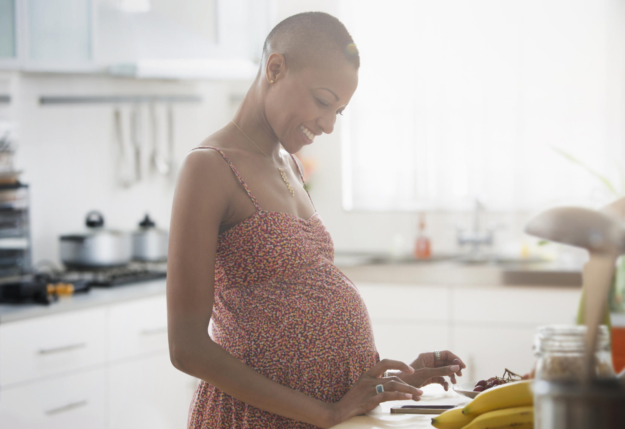 Pregnant Black woman using digital tablet in kitchen - stock photo