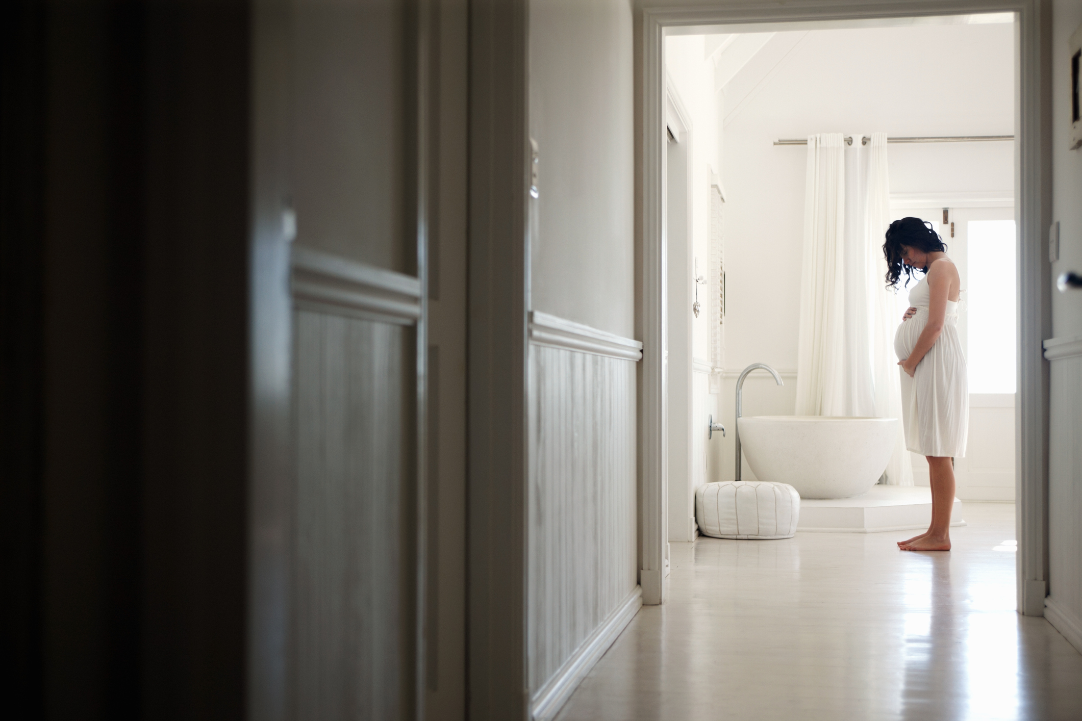 A pregnant woman holding her belly in a bathroom - stock photo