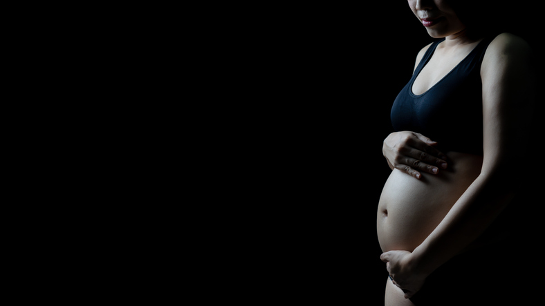 Midsection Of Pregnant Woman Touching Abdomen Against Black Background