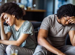 Young black couple feeling sad after arguing on sofa at home.