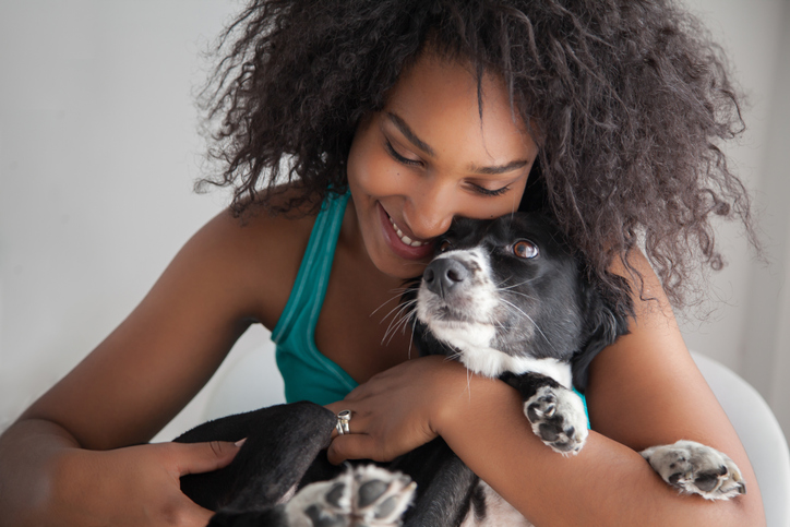Beautiful black woman hugging her mixed breed dog while she smiles
