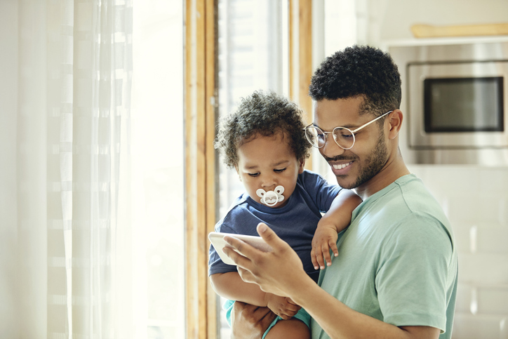 Father showing smart phone to son by window