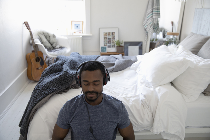 Serene young man meditating with headphones in bedroom