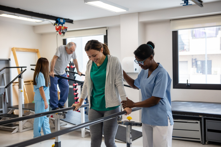 Group of people during physical therapy walking with the help of parallel bars at a rehab medical center