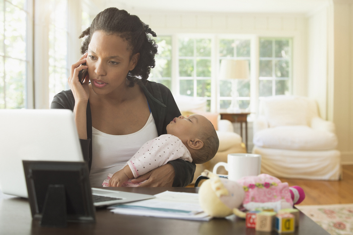 Mother holding baby and working in living room