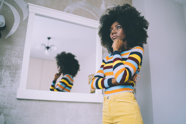 African woman standing pensive in front of a mirror