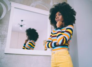 African woman standing pensive in front of a mirror