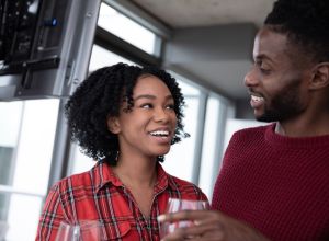 Young and happy black couple celebrating inside their condominium with red wine.