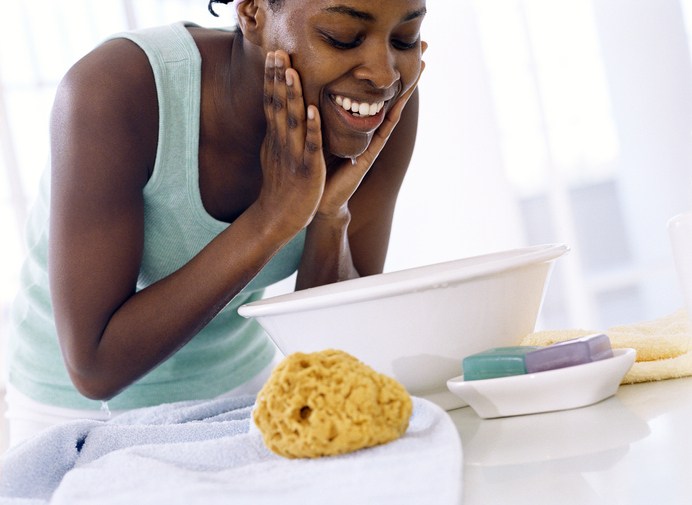 Young woman bent over bowl, washing face, smiling