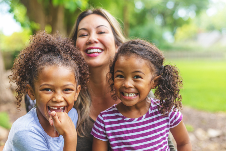 Asian Chinese Mother with two daughters of mixed Chinese and African American ethnicity in a green lush back yard setting posing for portraits smiling and being silly