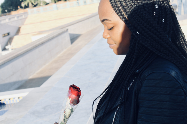 Young Woman Looking At Red Rose In City