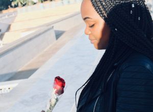 Young Woman Looking At Red Rose In City