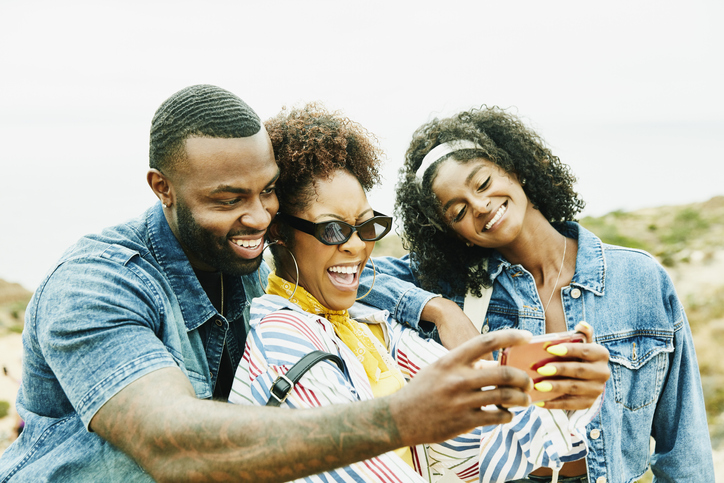 Smiling and laughing friends taking selfie with smart phone while exploring park