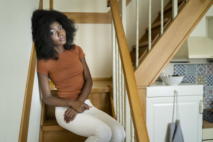 Sad african woman sitting on stairs at home