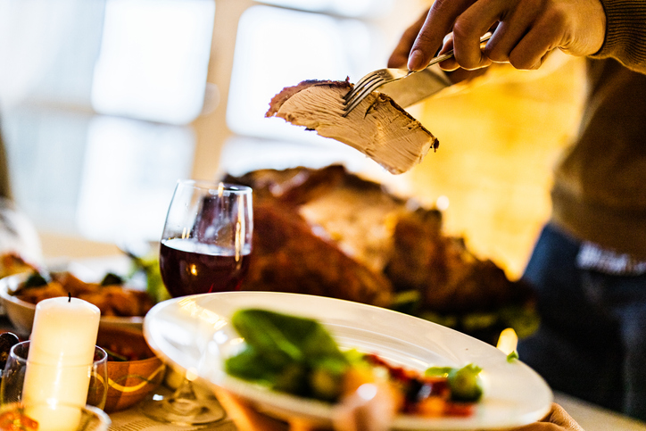 Unrecognizable man carving turkey meat and putting it on a plate at home.