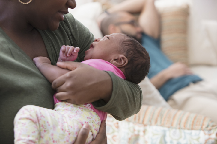 Afro-american woman holding her newborn baby while father sleeps