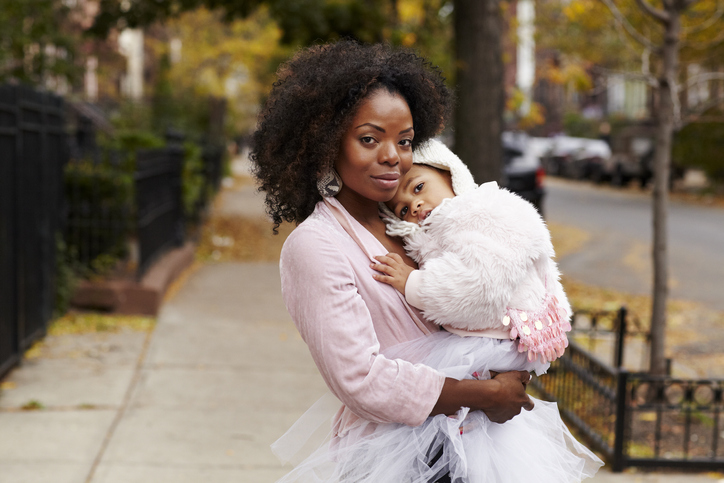 Black mother carrying daughter on city street