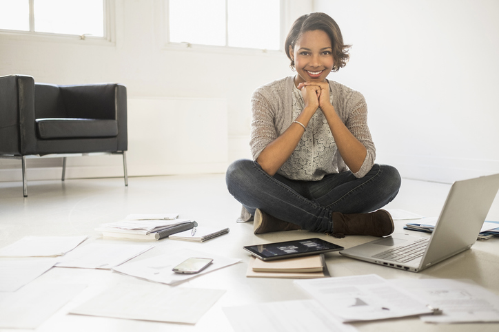 Black businesswoman smiling with laptop and digital tablet on floor