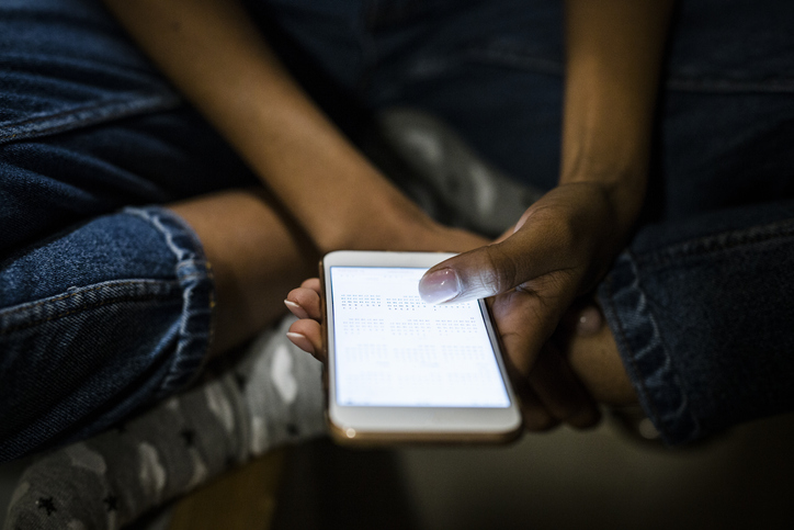 Young woman sitting at home, holding illuminated smartphone at night