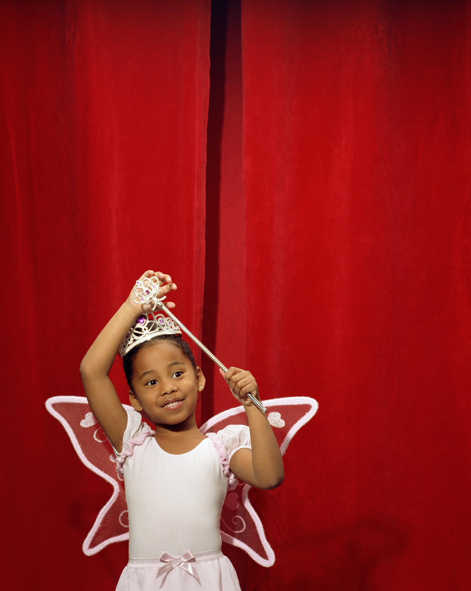 Girl (5-7) wearing fairy costume in front of red curtain