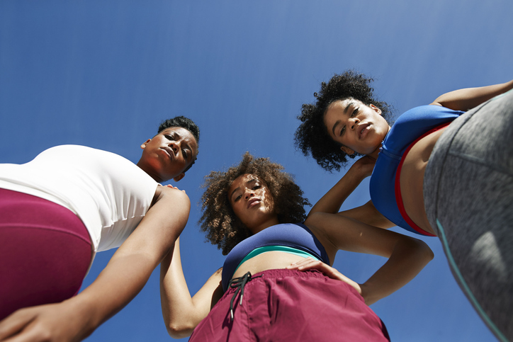 Portrait of female athletes in sportswear against blue sky