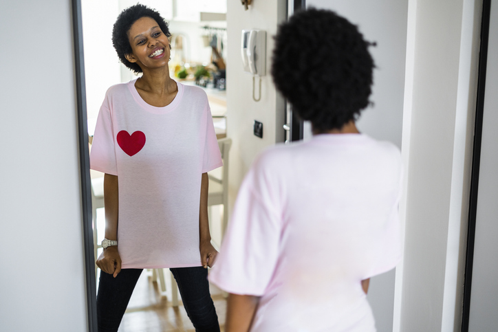 Happy young woman wearing t-shirt with heart shape looking in mirror