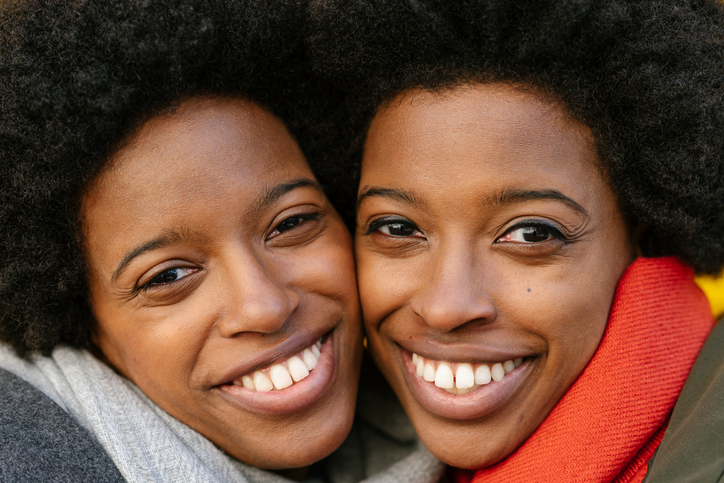 Portrait of happy twin sisters in front of yellow background