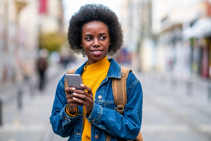 Cheerful female traveler using smart phone in the city.