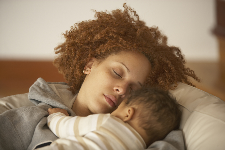 African American mother sleeping on sofa with baby